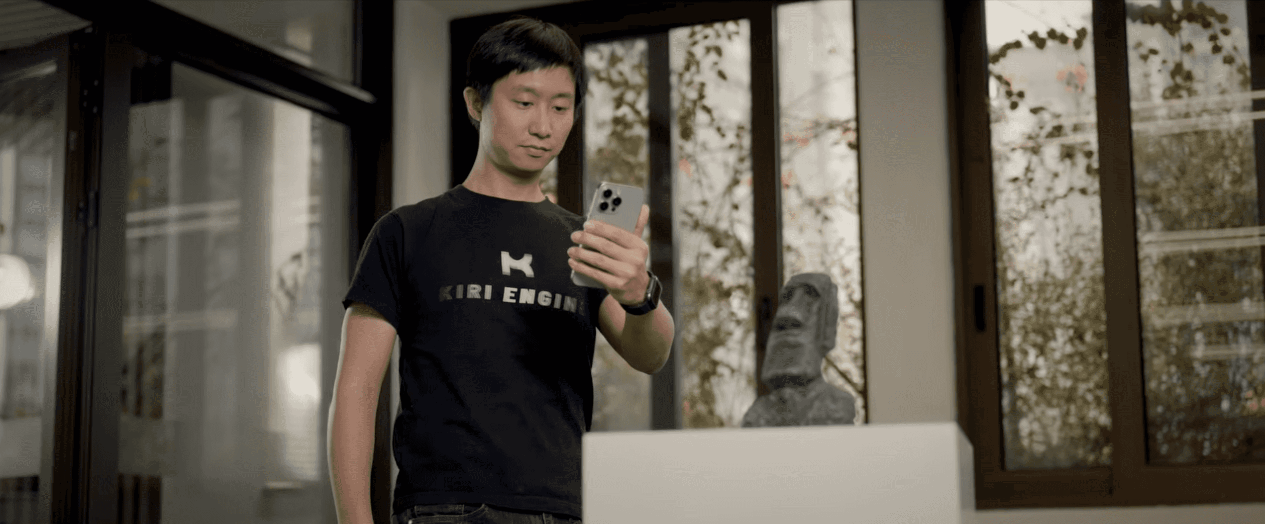 Person wearing a KIRI Engine t-shirt holding an iPhone Pro, scanning  a Moai statue figurine using KIRI Engine's 3DGS Scan mode