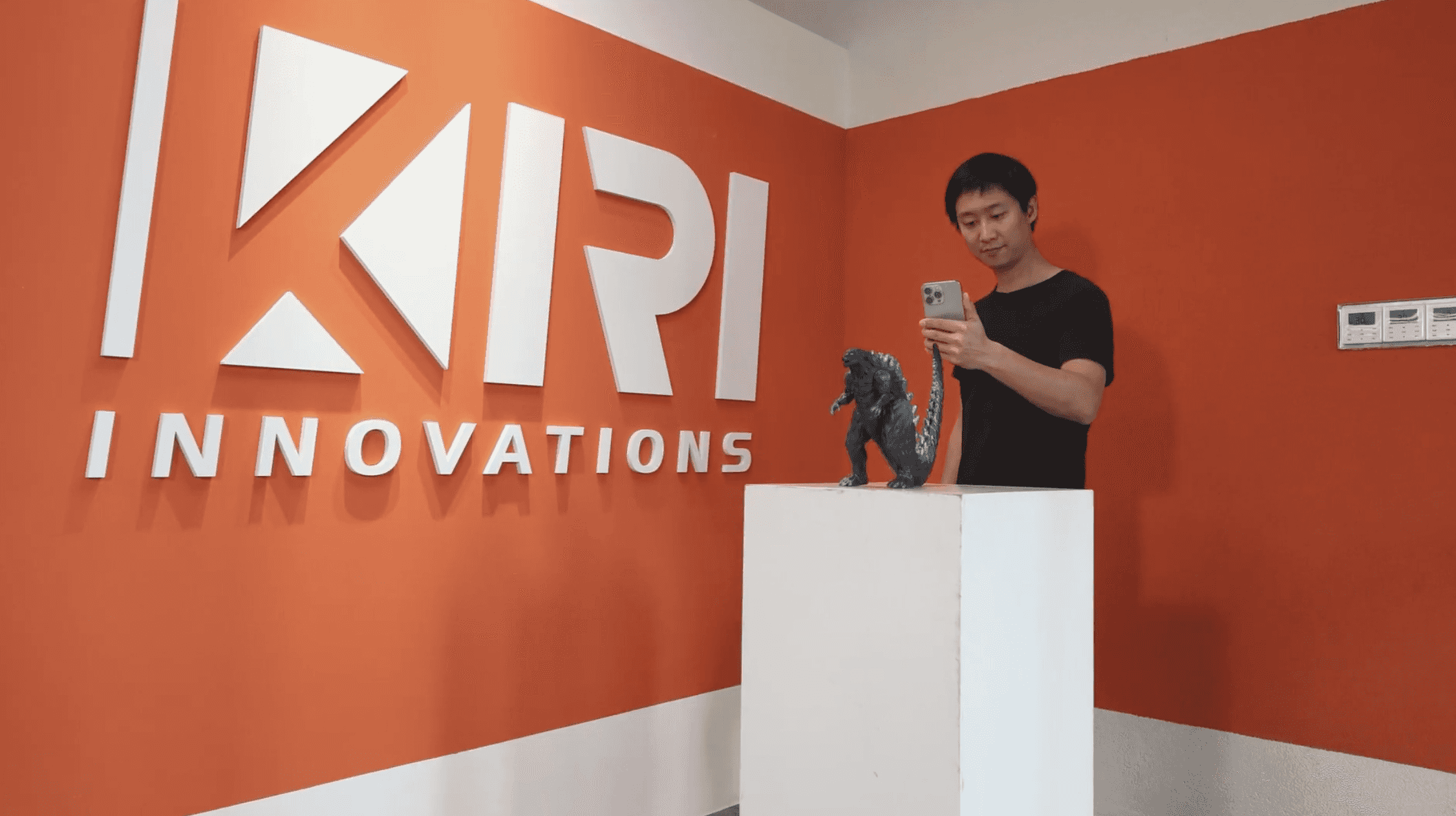 A person using a phone to capture a 3D object in front of a KIRI Innovations wall.